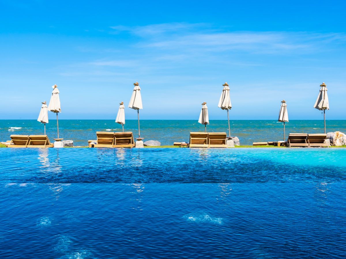 A resort infinity pool with sun loungers and umbrellas beside the sea
