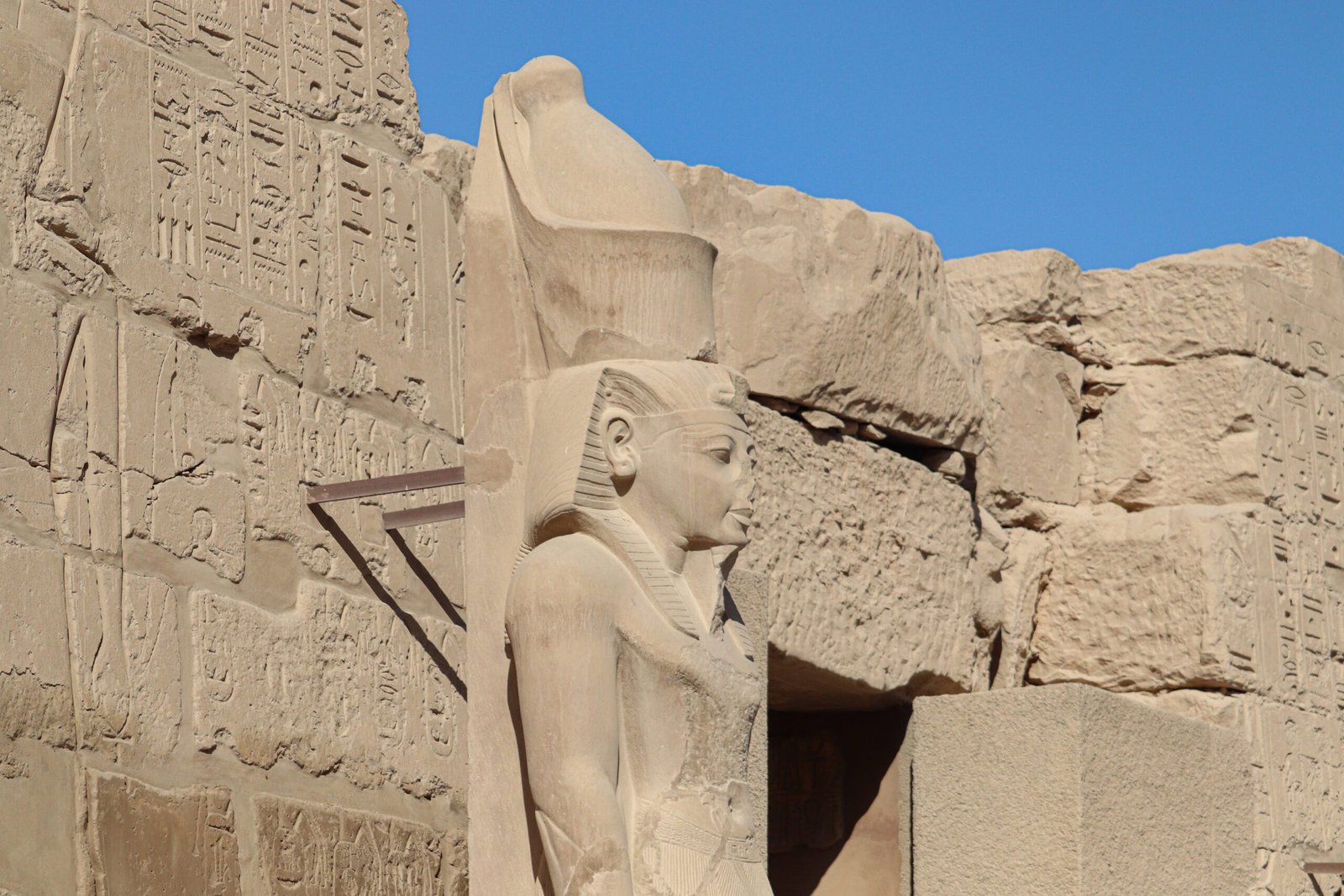 Egyptian queen stands front wall with stone wall building with large statue Egyptian queen.